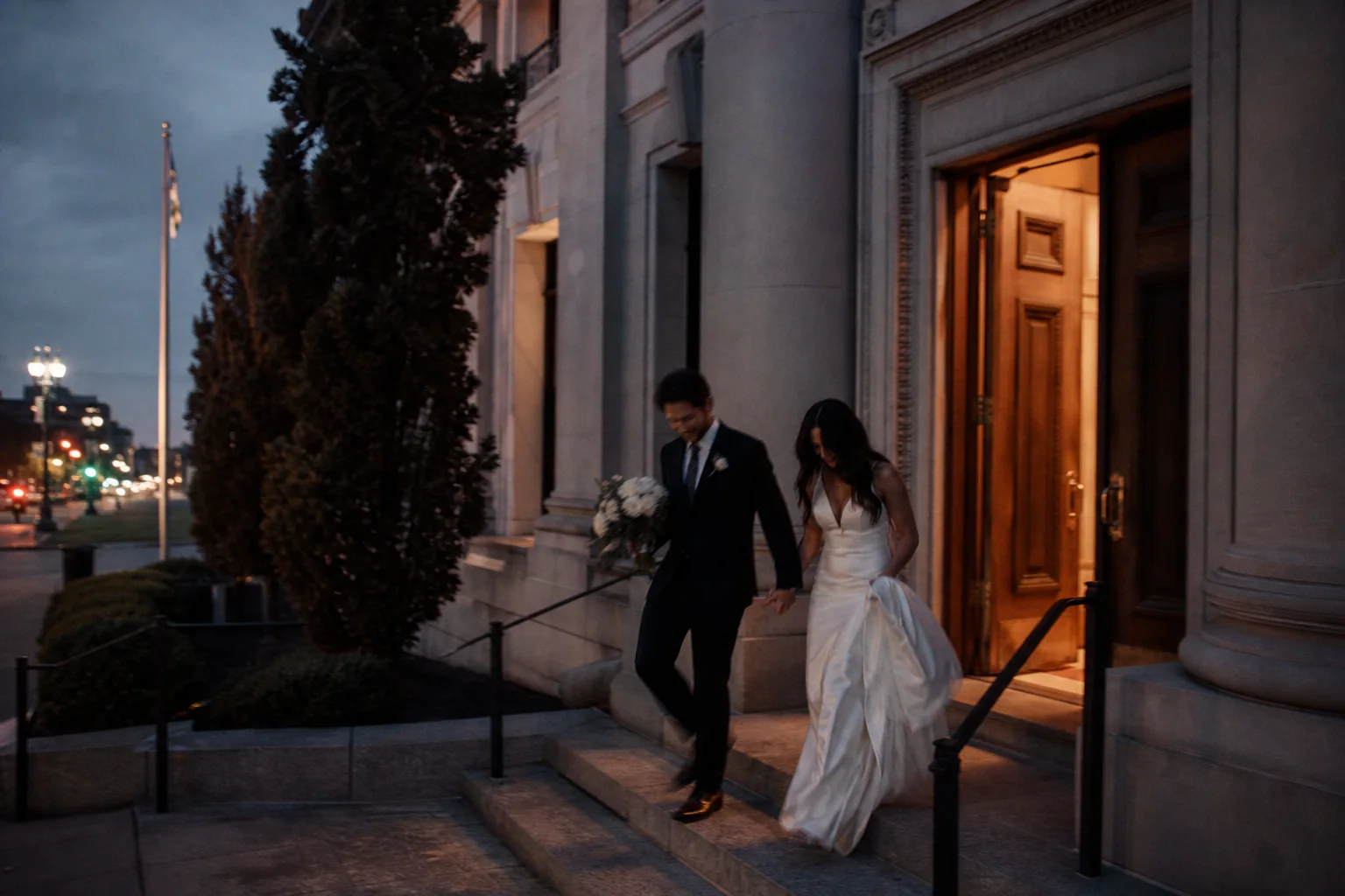 Newlyweds leaving a stone courthouse at dusk